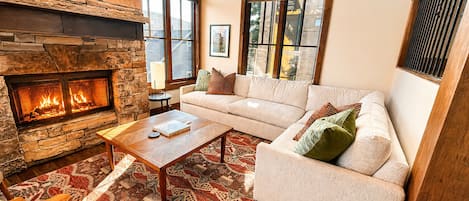 A cozy living room with a stone fireplace, a sofa, a coffee table, and a patterned rug.
