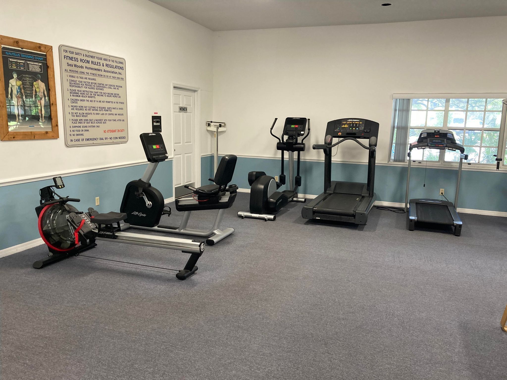 Une salle de remise en forme équipée d’appareils de cardio, d’un rameur et d’un panneau affichant les règles de sécurité.