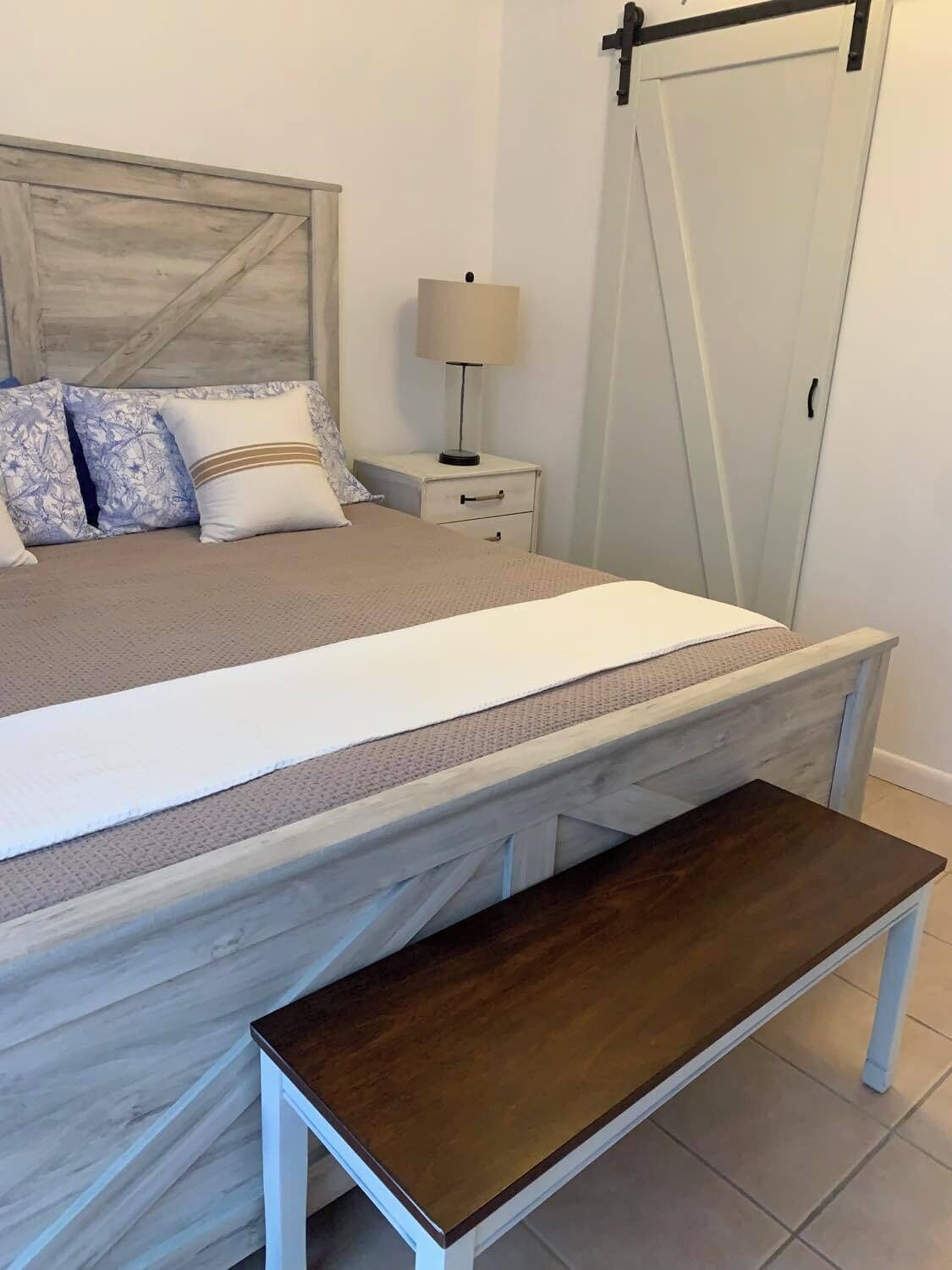 Ein Schlafzimmer mit Bett, Nachttisch, Lampe und einer Bank.