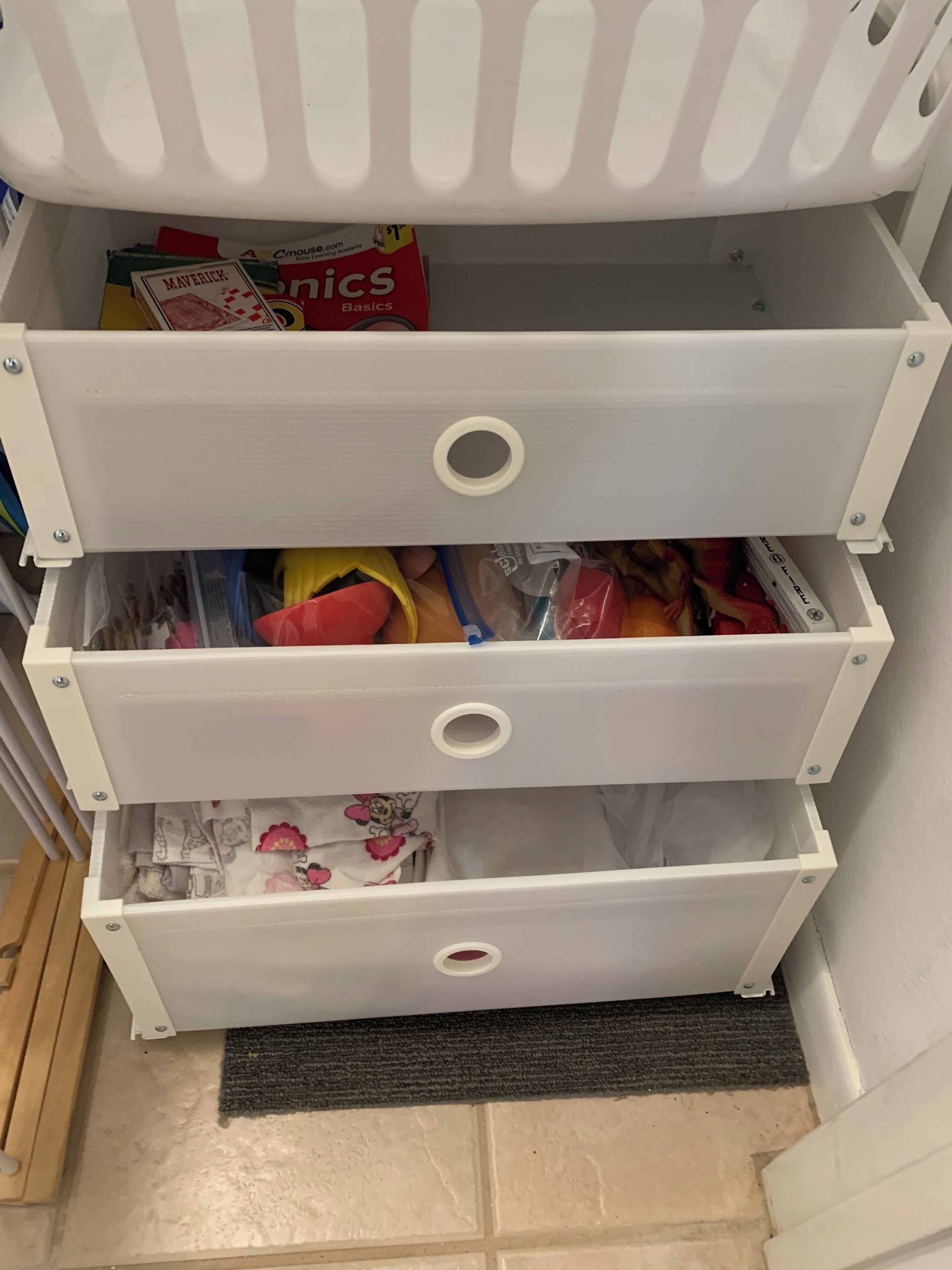 Un mueble blanco con tres cajones, cada uno con diversos objetos.