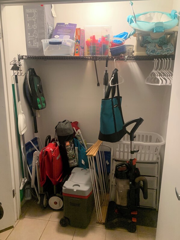 A storage area with shelves holding various items including a stroller, a vacuum cleaner, and cleaning supplies.