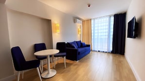 A modern living room with a blue sofa, two armchairs, a small round table, and a flat-screen TV mounted on the wall. - Orbi City C Block 2-room Apt 27fl Sea-mount View (Batumi)