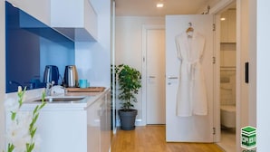 A modern kitchen with a sink, kettle, and potted plant. A white robe hangs on the door, and a sign for Orbi Group is visible. - Orbi City C Block 2-room Apt 27fl Sea-mount View (Batumi)