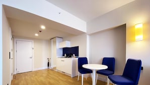 A modern kitchen with white cabinets and a small island, a dining area with a white table and blue chairs, and a wooden floor. - Orbi City C Block 2-room Apt 27fl Sea-mount View (Batumi)