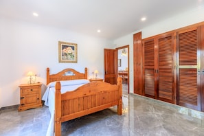 A bedroom with a wooden bed, a nightstand with a lamp, a dresser, and a large wooden wardrobe. - Juanito (Puerto Pollensa)