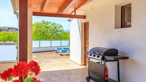 Un patio con una barbacoa, vistas a un lago y un balcón con una silla.