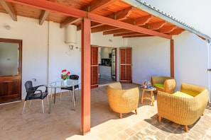 A covered patio area with wicker furniture, a glass table, and a view into the kitchen. - Juanito (Puerto Pollensa)