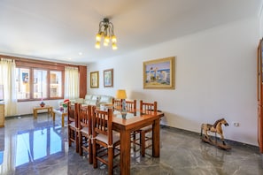 A spacious living area with a dining table, chairs, a sofa, and a painting on the wall. - Juanito (Puerto Pollensa)