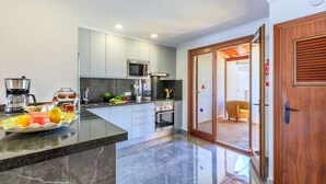 Una cocina moderna con encimera de mármol, electrodomésticos de acero inoxidable y una puerta de madera que da a un comedor.