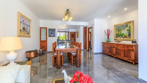 Un comedor amplio con una mesa y sillas de madera, una araña y vista a la cocina.
