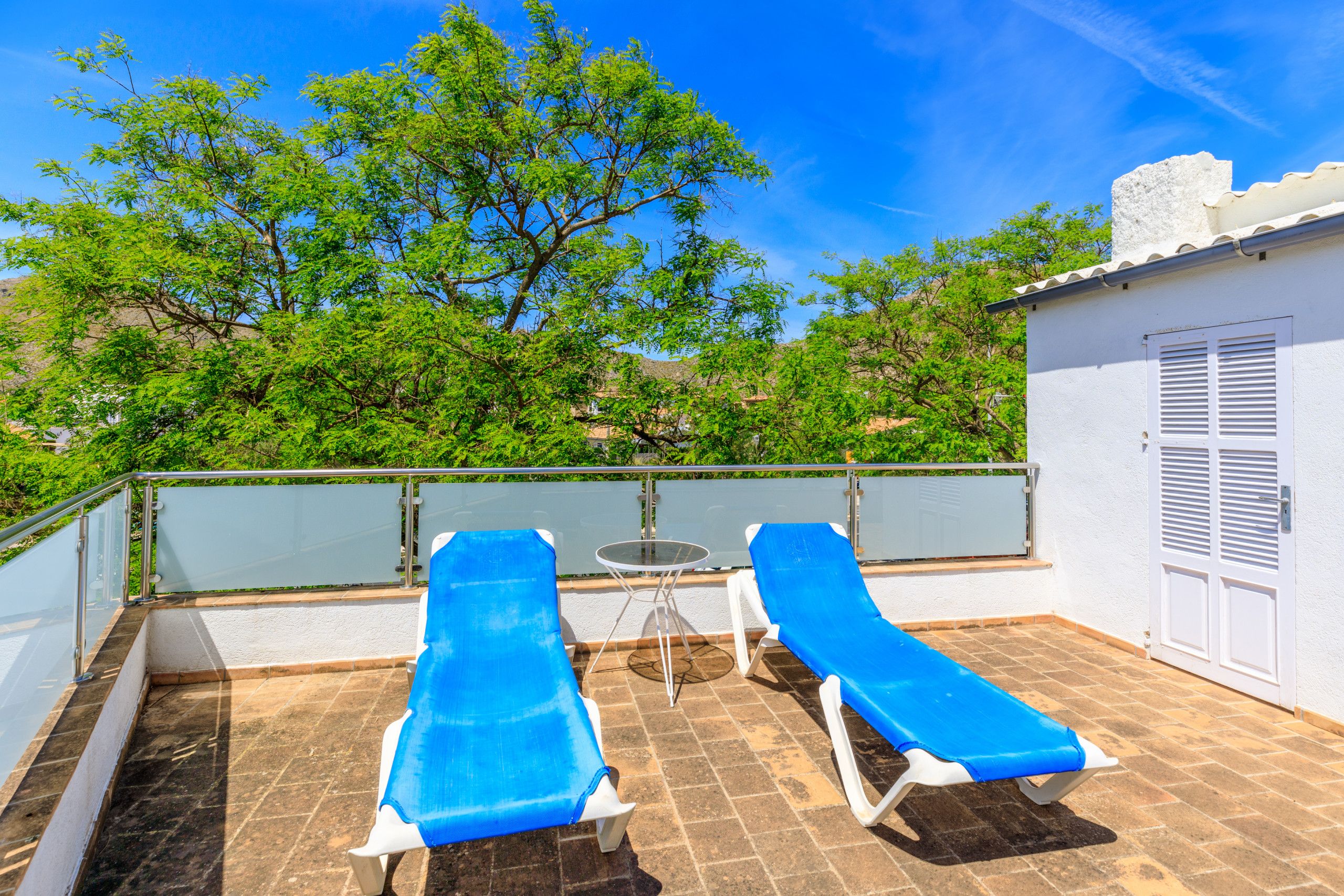 A balcony with two blue lounge chairs, a small round table, and a white door.