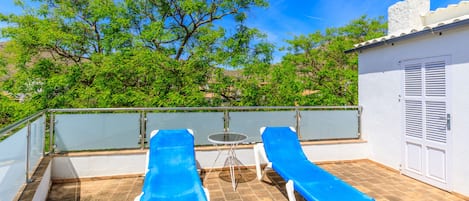 A rooftop terrace with two sun loungers, a small table, and a white door.