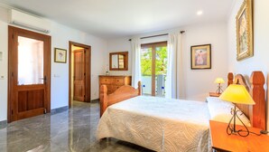 A hotel room with a bed, a wooden dresser, a desk with a lamp, a mirror, and a door leading to a balcony. - Juanito (Puerto Pollensa)