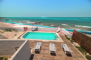 A pool with a view of the ocean, lounge chairs, and a wooden deck. - Hotel La Trigueña (Isla Mujeres)