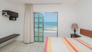 A bedroom with a bed, a nightstand, a lamp, a hanging coat rack, a sliding glass door to the balcony, and a small shelf. - Hotel La Trigueña (Isla Mujeres)