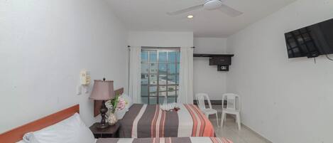 A hotel room with two beds, a ceiling fan, a TV, a desk, a chair, and a window with curtains.