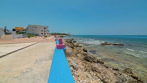 A coastal walkway with a blue path, rocky shoreline, and buildings in the background. - Hotel La Trigueña (Isla Mujeres)