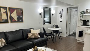 A modern living room with a black leather sofa, a round coffee table, and a dining area with a white table and black chairs.