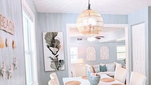 Un espace repas avec une table et des chaises blanches, un lustre et des œuvres d’art murales.