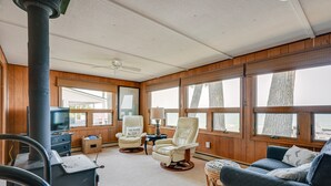 A cozy cabin interior with a wood-paneled wall, a fireplace, a television, a comfortable chair, and a sofa. - 'Summer Place' A Vibrant Rental on Lake Huron (Tawas City)