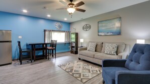 A modern living room with a blue accent wall, a dining area with a wooden table and chairs, a beige sofa, and a ceiling fan.
