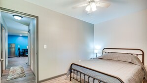 A bedroom with a bed, a ceiling fan, and a visible hallway leading to a kitchen area.