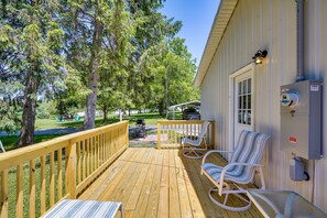 Une terrasse en bois avec deux chaises à rayures et une table, un barbecue et un coffret électrique sur le côté d’une maison.
