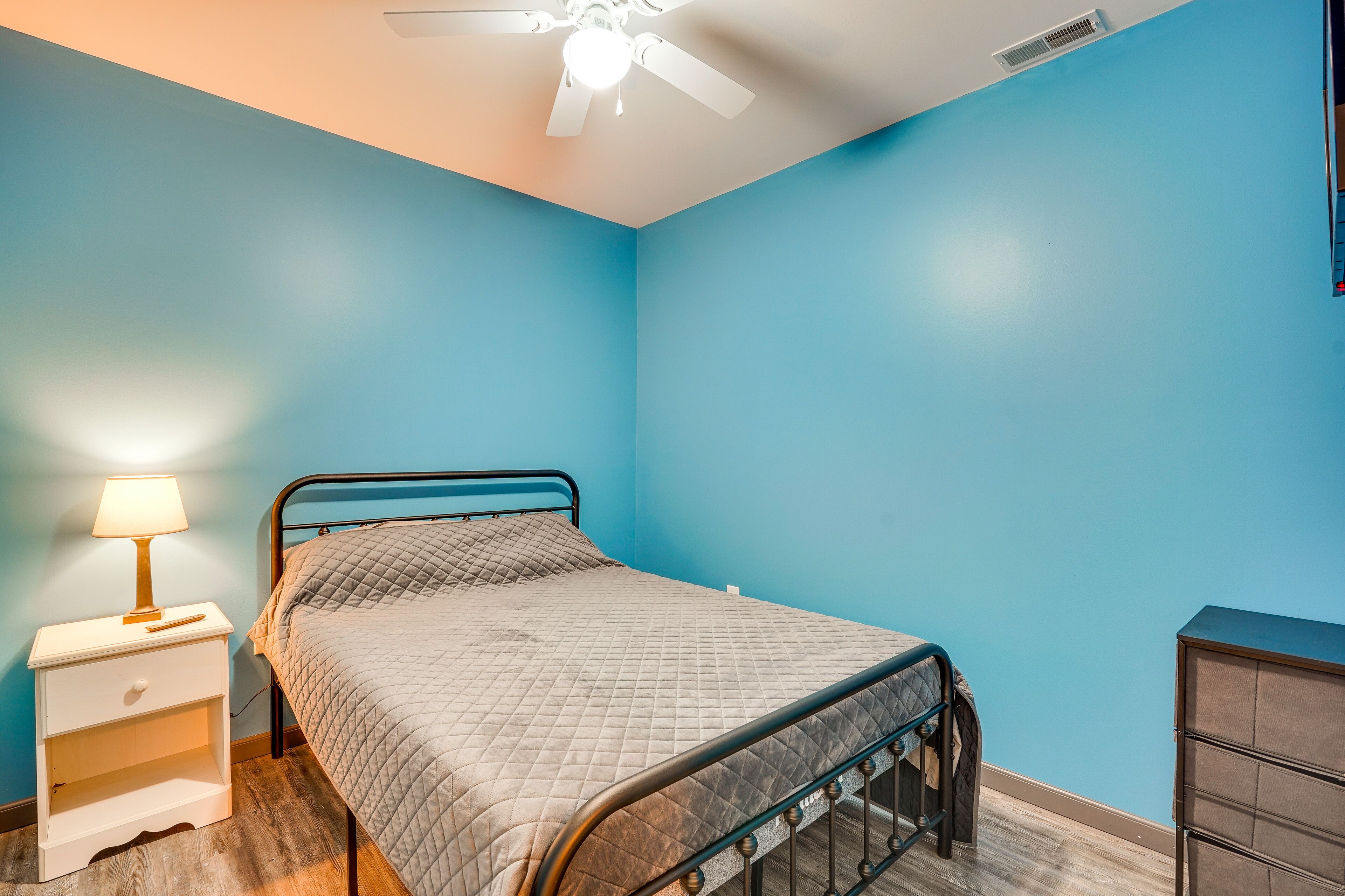 Une chambre à coucher comprenant un lit, une table de chevet, une commode et un ventilateur de plafond.