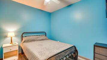 Une chambre à coucher comprenant un lit, une table de chevet, une commode et un ventilateur de plafond.