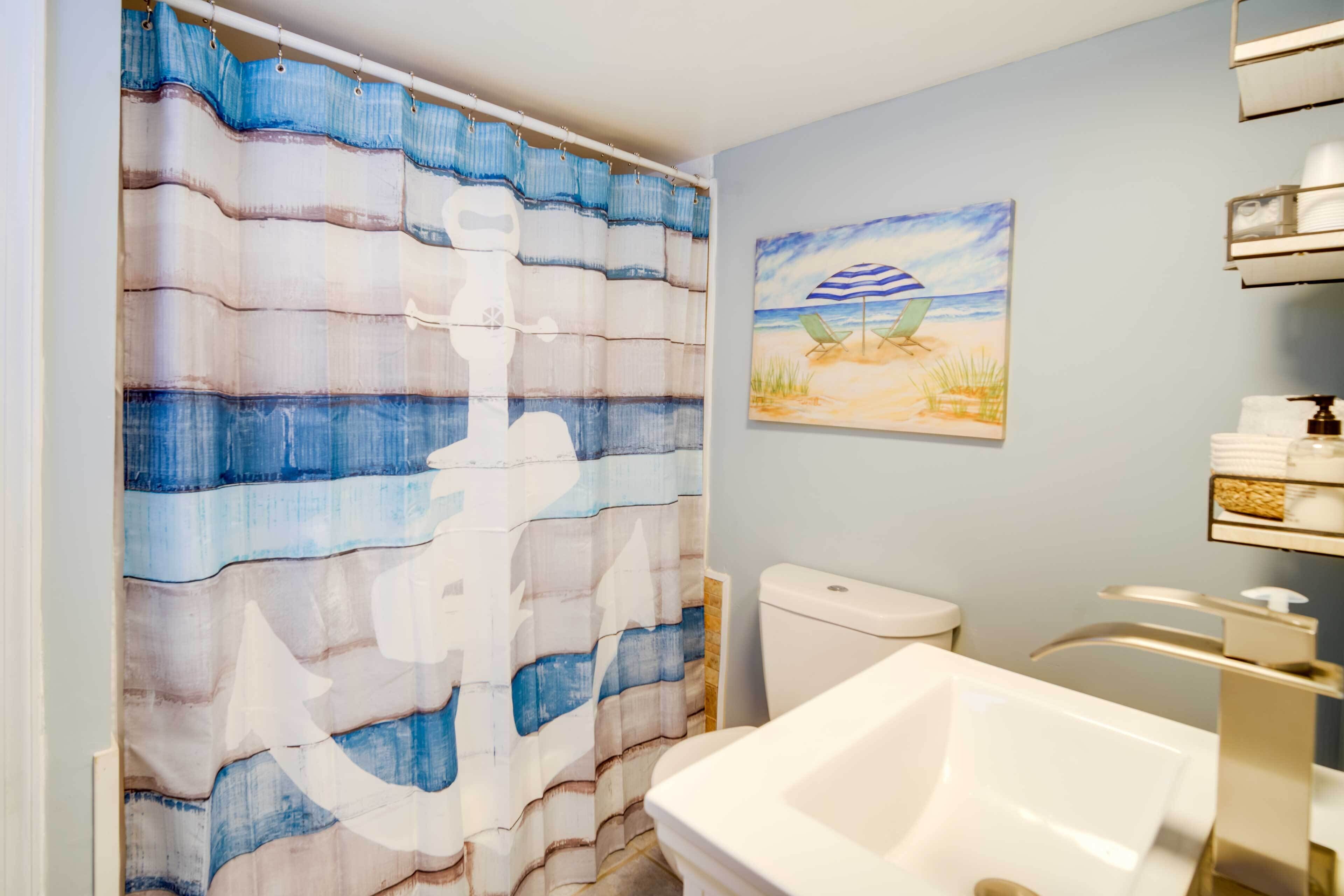 A bathroom with a striped shower curtain, a toilet, a sink with a modern faucet, and a beach-themed painting on the wall.