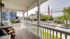A covered porch with a view of a street, a building with a flag, and outdoor seating. - Charming Ocean City Apartment < 1 Mi to Boardwalk! (Ocean City)