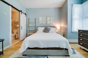 Een slaapkamer met een bed, nachtkastje, dressoir, ladder en inloopkast.