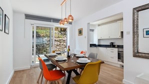 A modern dining area with a wooden table, orange and yellow chairs, and a view of a stone garden through glass doors.