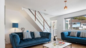 A modern living room with two blue sofas, a coffee table, and a staircase.
