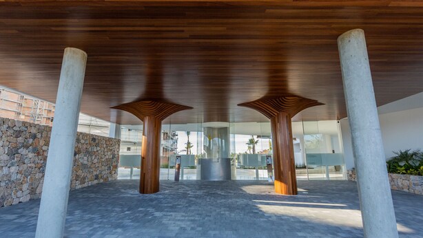 Una estructura arquitectónica moderna con techo de madera y pilares de hormigón.