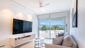 Una sala de estar moderna con un televisor de pantalla plana, un sofá, un ventilador de techo y un balcón con vistas a las montañas.