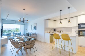 A modern kitchen with white cabinets, a central island with bar stools, and a dining area with a glass table and wicker chairs.