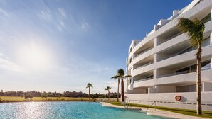 Un hotel moderno con piscina, palmeras y cielo despejado.