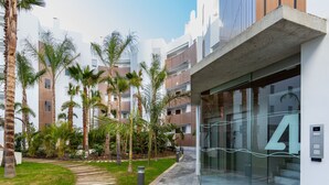 Un edificio moderno con entrada de vidrio, palmeras y un sendero que lleva a la entrada.