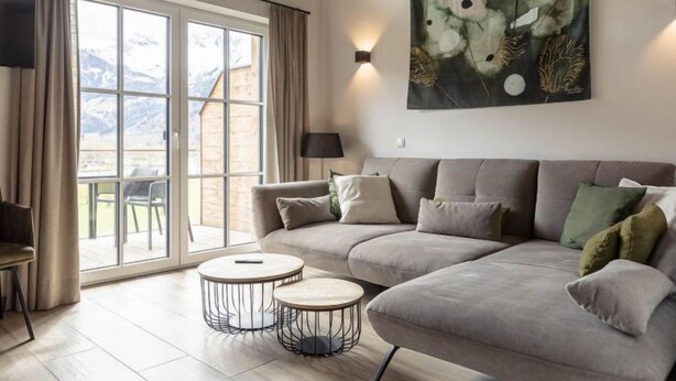A modern living room with a grey sofa, two round coffee tables, a large abstract painting, a TV, and a view of mountains through large windows. - Superior # 2B mit Sauna by Interhome (Uttendorf)