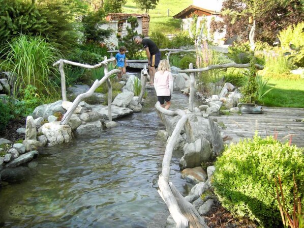 A naturalistic garden with a stream, wooden bridges, and lush greenery.