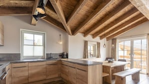 A spacious kitchen with wooden cabinets and a large island, featuring a window and a view of the outdoors. - Superior # 4D mit Sauna by Interhome (Uttendorf)