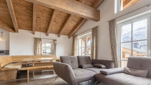 A modern living room with a wooden ceiling, a grey sofa, a wooden bench, and a round coffee table. - Superior # 4D mit Sauna by Interhome (Uttendorf)