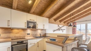 Une cuisine moderne avec des poutres en bois, des armoires blanches, des appareils électroménagers en acier inoxydable et un coin bar avec des sièges.