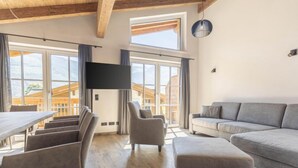 Un espacio habitable amplio con un gran ventanal, un televisor de pantalla plana, un sofá gris y una mesa de comedor con sillas.