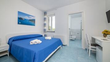 Habitación de hotel con cama, escritorio, silla, baño y un cuadro de una escena costera.