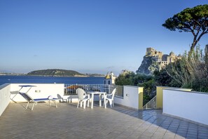 Una terraza con mesa y sillas, con vistas a una zona costera donde se alza un castillo en un acantilado.