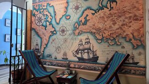 A room with a large map on the wall, two striped chairs, a small table with books, and a potted plant. - Amura Hostel  (Antigua Guatemala)