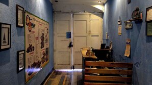 A hallway with a blue wall, wooden bench, framed pictures, and a bulletin board. - Amura Hostel  (Antigua Guatemala)