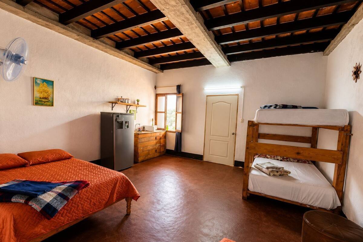 Une chambre de dortoir avec des lits superposés, un réfrigérateur, un petit coin cuisine et une fenêtre.